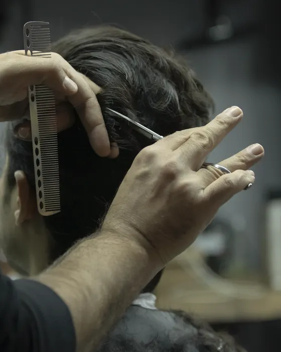 Coiffeur schneidet einem Kunden die Haare mit Kamm und Schere