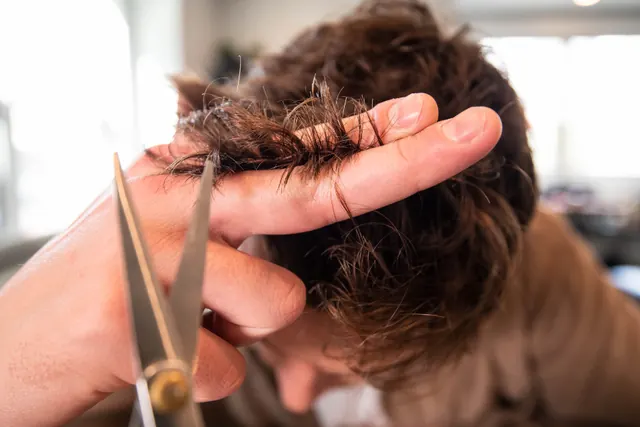 Haarschnitt mit der Schere, nah an den Händen der Coiffeur:in